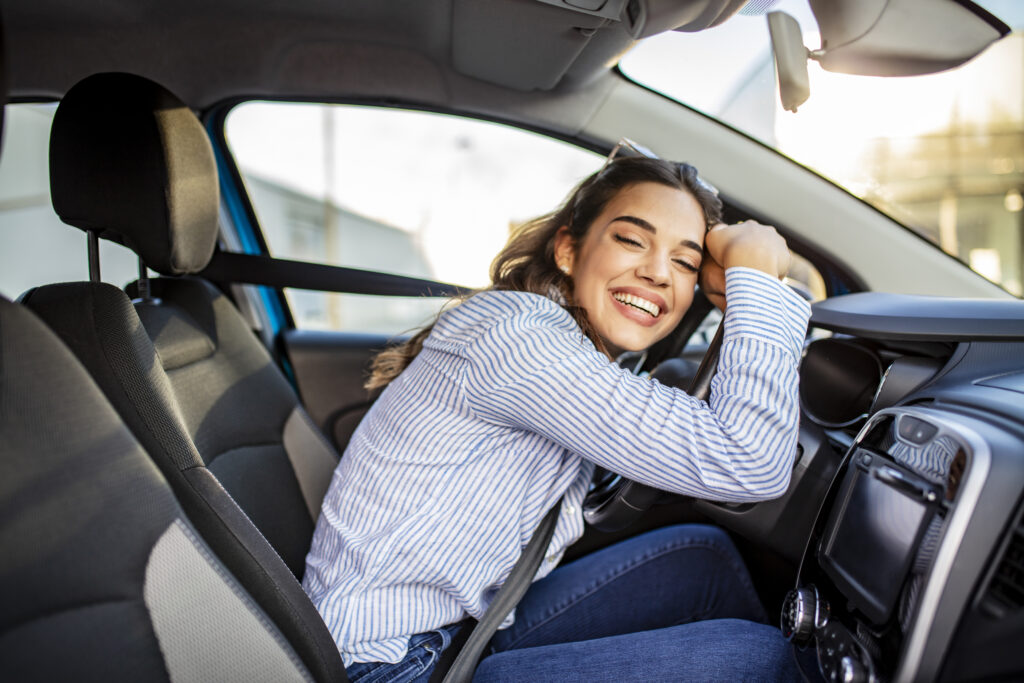 Young woman enjoying new car hugging steering wheel.