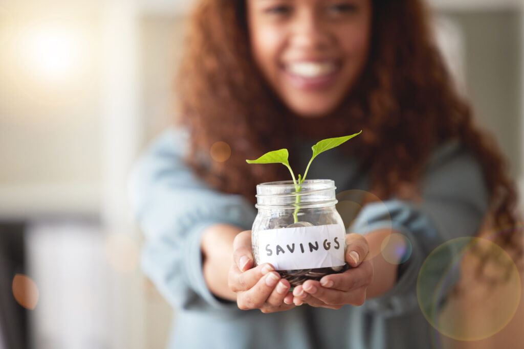 Young woman holding a glass savings jar with a budding plant growing out from it.